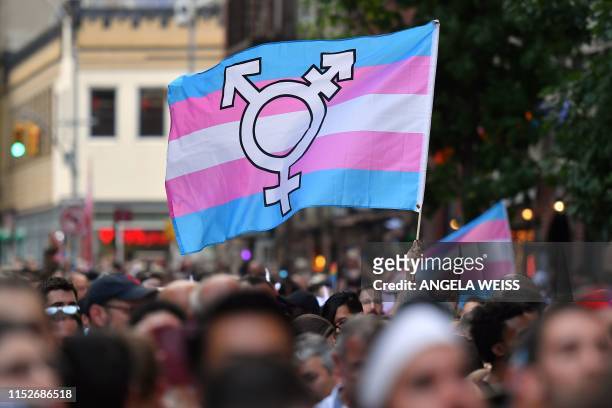 Person holds a transgender pride flag as people gather on Christopher Street outside the Stonewall Inn for a rally to mark the 50th anniversary of...