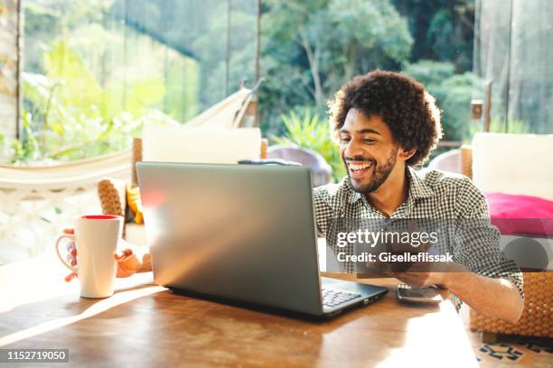 jeune homme utilisant l’ordinateur portatif dans le salon - brazilian ethnicity photos et images de collection