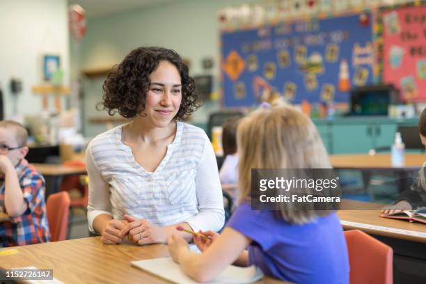 en första klass lärare pratar med en av hennes elever i klass rummet - lärare bildbanksfoton och bilder
