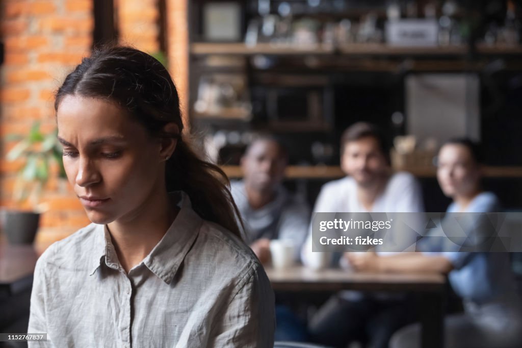 Upset mixed race woman suffering from bullying, sitting alone in cafe