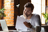 Confused frustrated man reading letter in cafe, receiving bad news