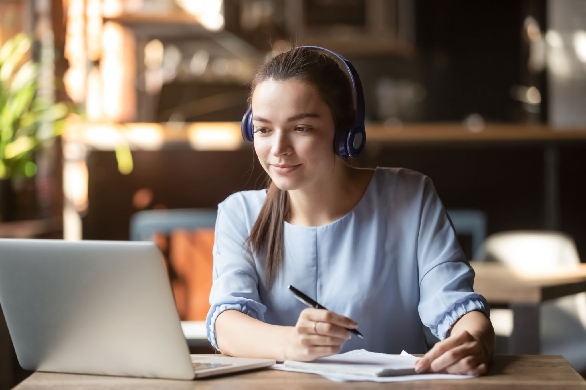 Focused woman wearing headphones using laptop, writing notes Focused woman wearing headphones using laptop, writing notes