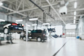 Repair service station with lifted modern cars being under maintenance and technicians on blurred background with many diode lamps. Auto service and technician concept