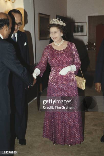 Queen Elizabeth II, wearing a four-strand diamond and pearl choker with the 'Girl's of Great Britain and Ireland' tiara, shaking hands with a guest...