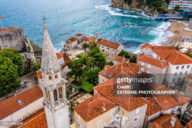 vista aérea de un campanario de la iglesia que se eleva desde los tejados del casco antiguo de budva, situado en la fortaleza mogren - montenegro fotografías e imágenes de stock