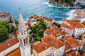 Aerial view of a Church bell tower rising from the rooftops of Old Town of Budva, situated on the Fortress Mogren