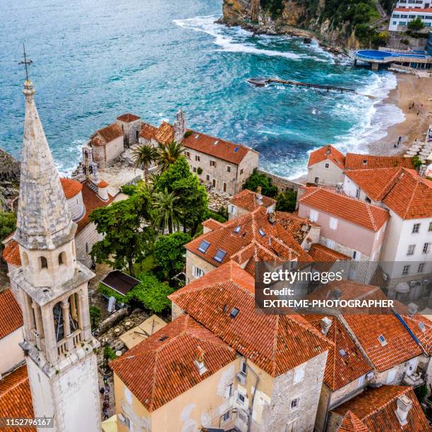 high angle view of a church tower and rooftops of old town of budva, and adriatic sea washing the coastline of montenegro - budva stock pictures, royalty-free photos & images