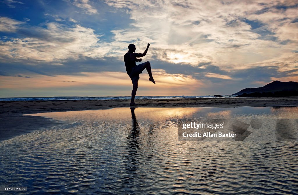 Silhouette of man practising kung fu moves on beach at sunset