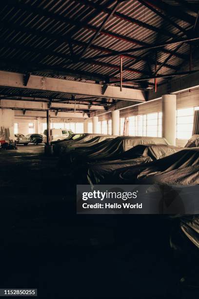 cars in storage warehouse under dust covers - werkstatt garage stock-fotos und bilder