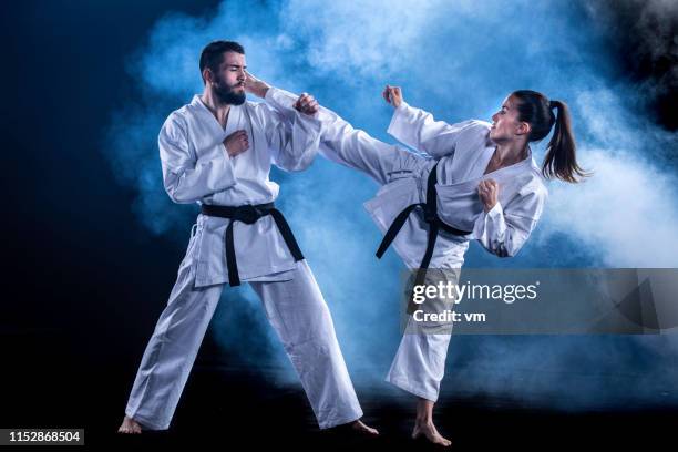 vrouwelijke karateka doen een draaiende kick op de mannelijke sparringpartner - duelleren stockfoto's en -beelden