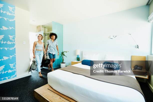 smiling lesbian couple walking into hotel room carrying luggage - lesbian bed stock pictures, royalty-free photos & images