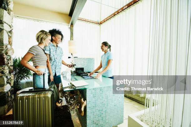 smiling lesbian couple using smart phone to pay while checking into hotel - checking in at hotel stock-fotos und bilder