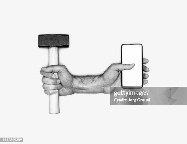 two hands holding a hammer and a smartphone - mobile phone evolution stock-fotos und bilder