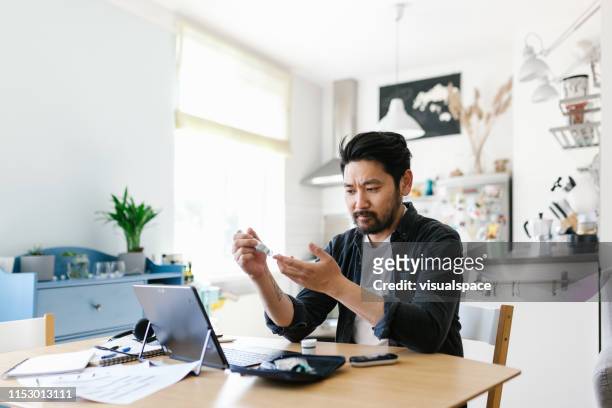 asian man checking blood sugar while working from home office - diabetes technology stock pictures, royalty-free photos & images