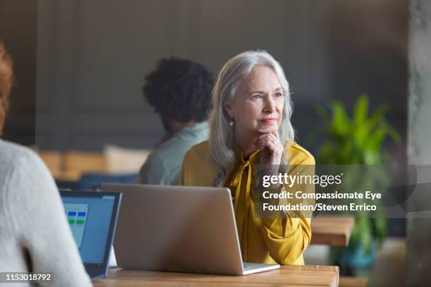 business woman using laptop in modern open plan office - older workers stock-fotos und bilder