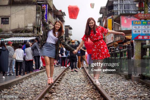 twee aziatische vrouwelijke toeristen houden handen en wandelen gelukkig langs railway in shefen, taiwan - taiwanese ethnicity stockfoto's en -beelden
