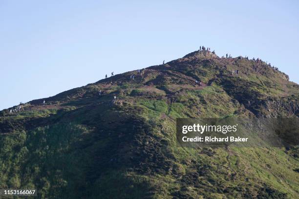 In summer evening sunshine, walkers climb the last metres to the summit of Arthur's Seat in Holyrood Park that overlooks the city of Edinburgh, on...