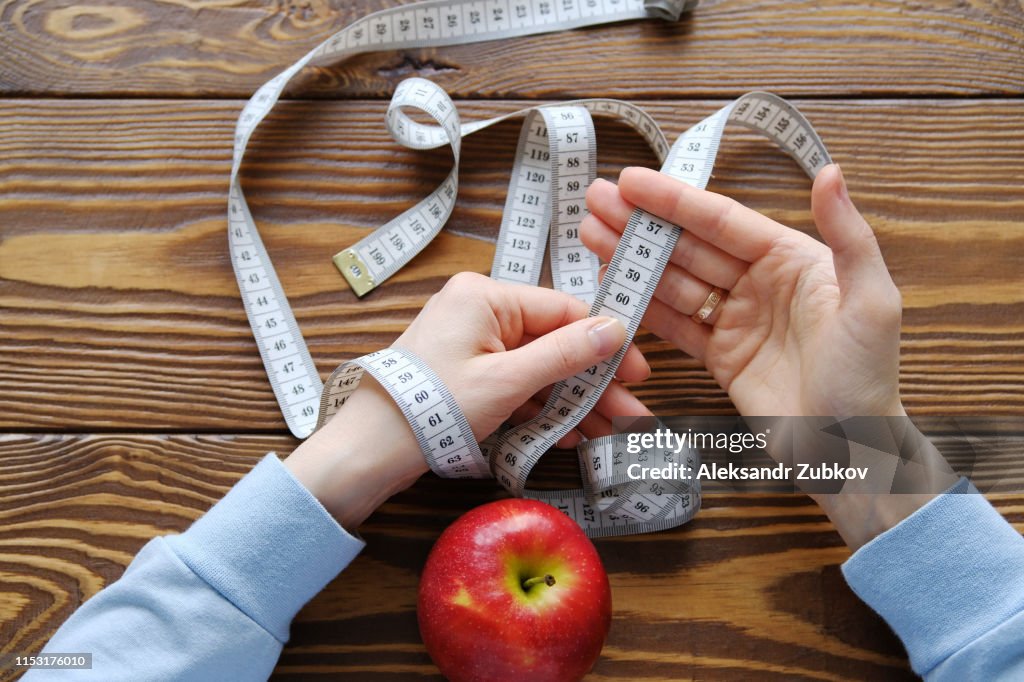 Women's hands holding measuring tape on a wooden background. The concept of diet, healthy lifestyle and proper nutrition. Copy space. Weight loss, weight loss, vegetarian diet. Minimalism in food