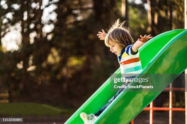 niedlicher junge genießen im öffentlichen park - slide stock-fotos und bilder