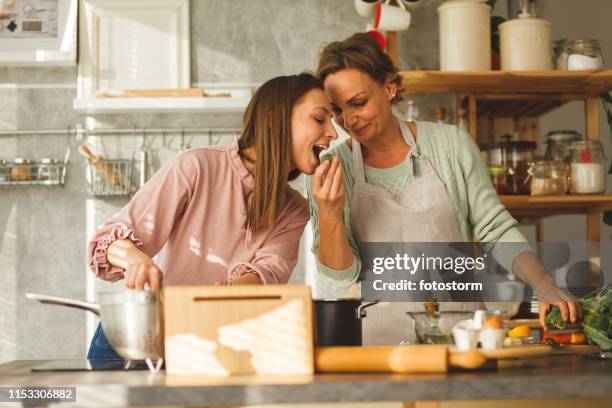 young woman tasting food her mother is preparing - mother daughter cooking stock pictures, royalty-free photos & images