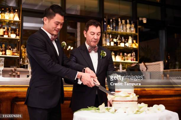 Homosexual couple cutting the wedding cake at the reception dinner.