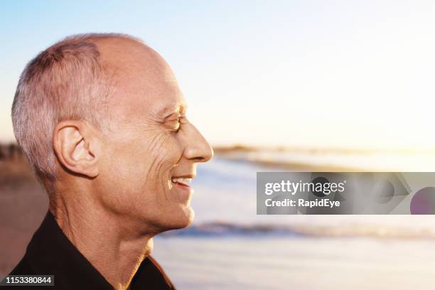 profile of senior man on beach, smiling happily in sunshine - human head bald stock pictures, royalty-free photos & images