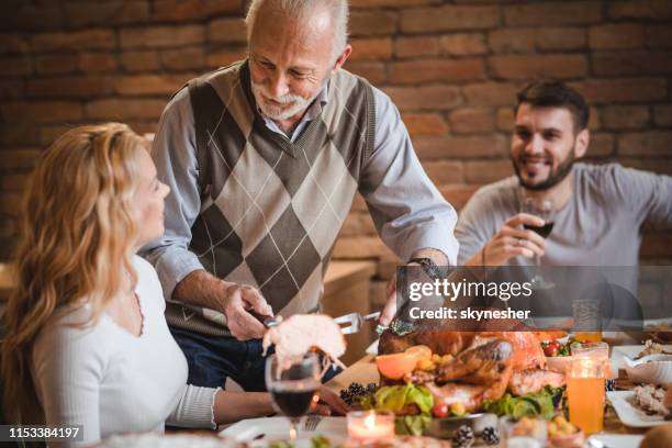 happy senior man serving thanksgiving turkey to his adult children in dining room. - daughter in law stock pictures, royalty-free photos & images