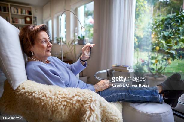 Senior woman resting in armchair at home holding cell phone