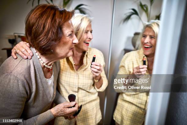 two happy senior women looking in mirror applying make-up - makeup mirror stock pictures, royalty-free photos & images
