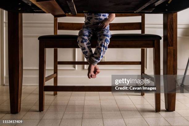 feet of young boy dangling off tall bench seen from underneath table - table leg stock pictures, royalty-free photos & images