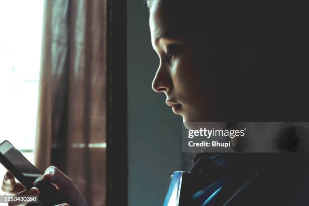 girl holding book and texting on mobile phone - unhappy school child stock pictures, royalty-free photos & images