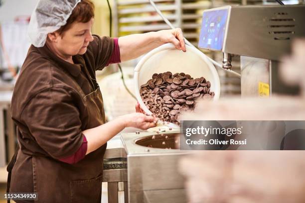 woman in a chocolate manufacture filling machine with chocolate pieces - chocolate pieces stock-fotos und bilder