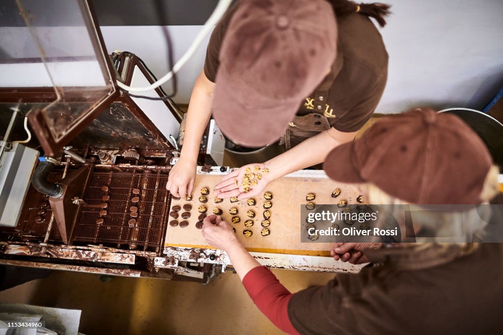 Two women in a chocolate manufacture placing walnuts on pralines