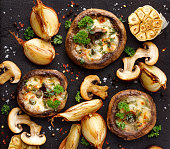 Roasted portobello mushrooms stuffed with cheese and herbs on a black iron  background, top view.
