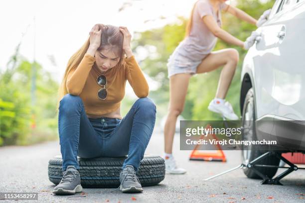 two young beautiful women and changing spare car tire on the road - happy client by broken car stock pictures, royalty-free photos & images