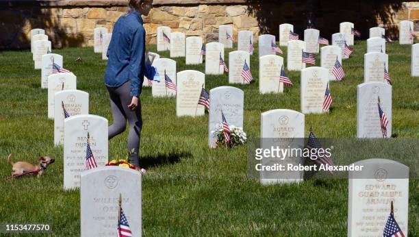 Young woman and her pet dog walk among the tombstones at the Santa Fe National Cemetery on Memorial Day. The cemetery, in Santa Fe, New Mexico, is...