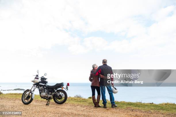 retired couple on a motorbike ride along a coastal road - mare moto foto e immagini stock