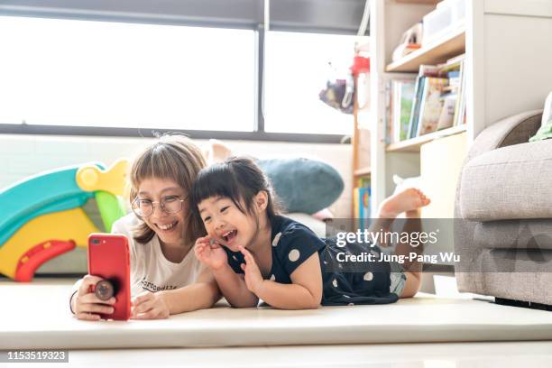 mother taking selfie with cellphone happily with young daughter - chinese family taking photo at home stock pictures, royalty-free photos & images