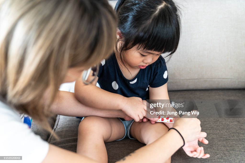 Mother applying adhesive bandage for young daughter