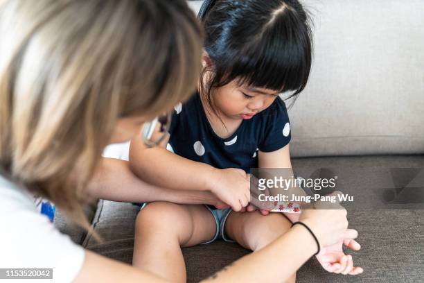 mother applying adhesive bandage for young daughter - pleister stockfoto's en -beelden