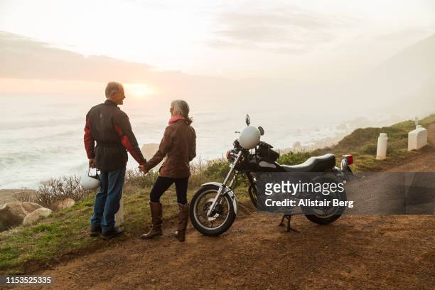 retired couple on a motorbike ride on a coastal road - mare moto foto e immagini stock