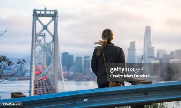 young woman looking at san francisco skyline and bay bridge - treasure island san francisco stock pictures, royalty-free photos & images