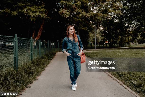 happy young woman enjoying a walk in the park - jumpsuit stock pictures, royalty-free photos & images