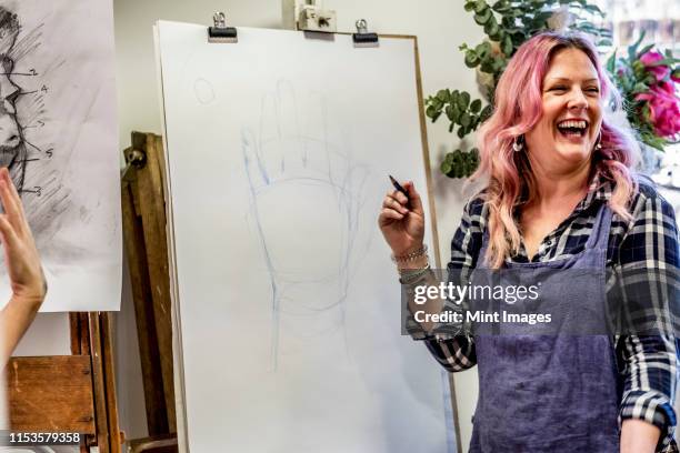 laughing woman wearing apron standing at an easel, drawing of human hand. - art class stock pictures, royalty-free photos & images