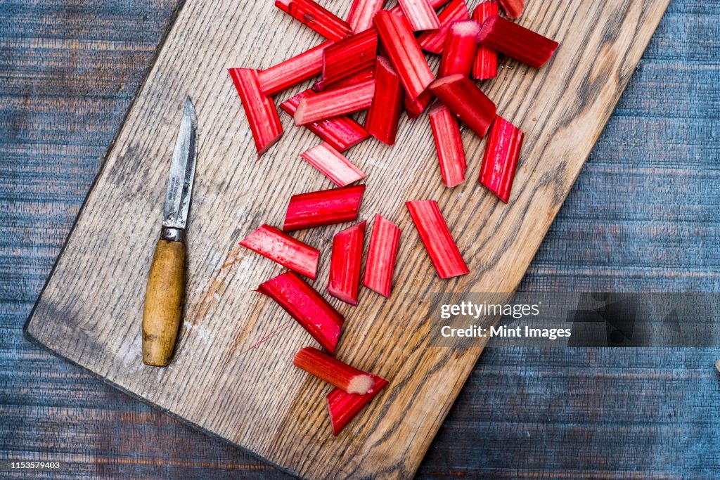 High angle close up of slices of rhubarb and knife on wooden cutting board.