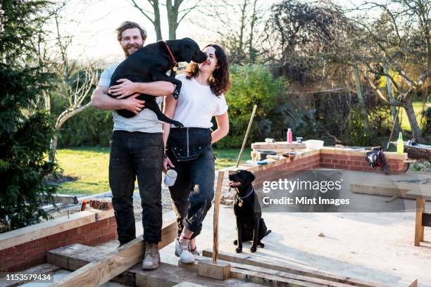 smiling man and women and two black dogs on building site of residential building. - artisan portrait equipe photos et images de collection