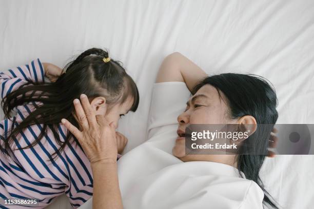 thaise oma onderwijs haar baby op bed - ear close up women stockfoto's en -beelden