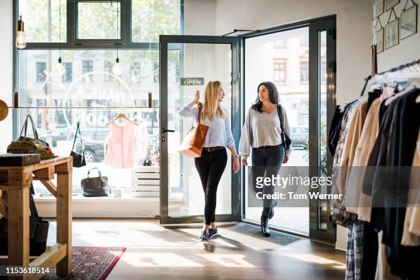 two women entering clothing store together - entrando fotografías e imágenes de stock