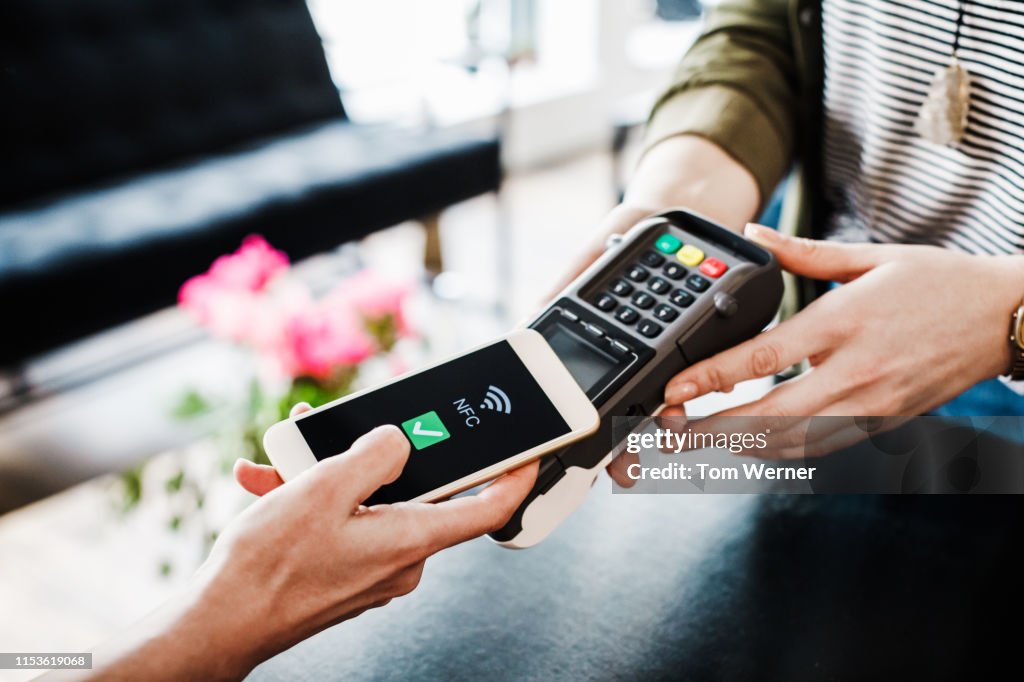 Close Up Of Woman Using Smartphone To Pay For Shopping