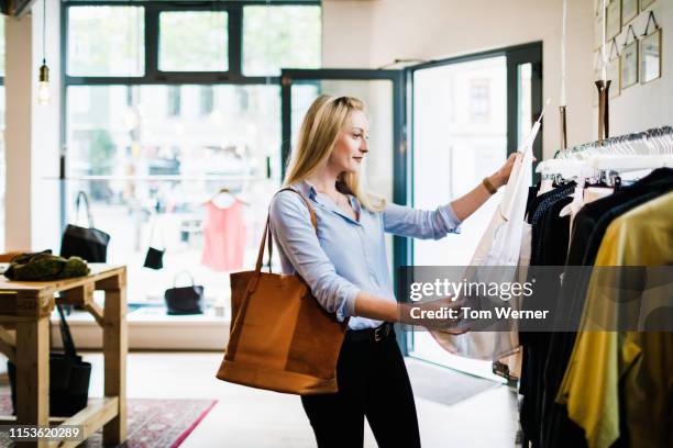 woman looking at blouse while shopping for the day - clothes shop stock pictures, royalty-free photos & images